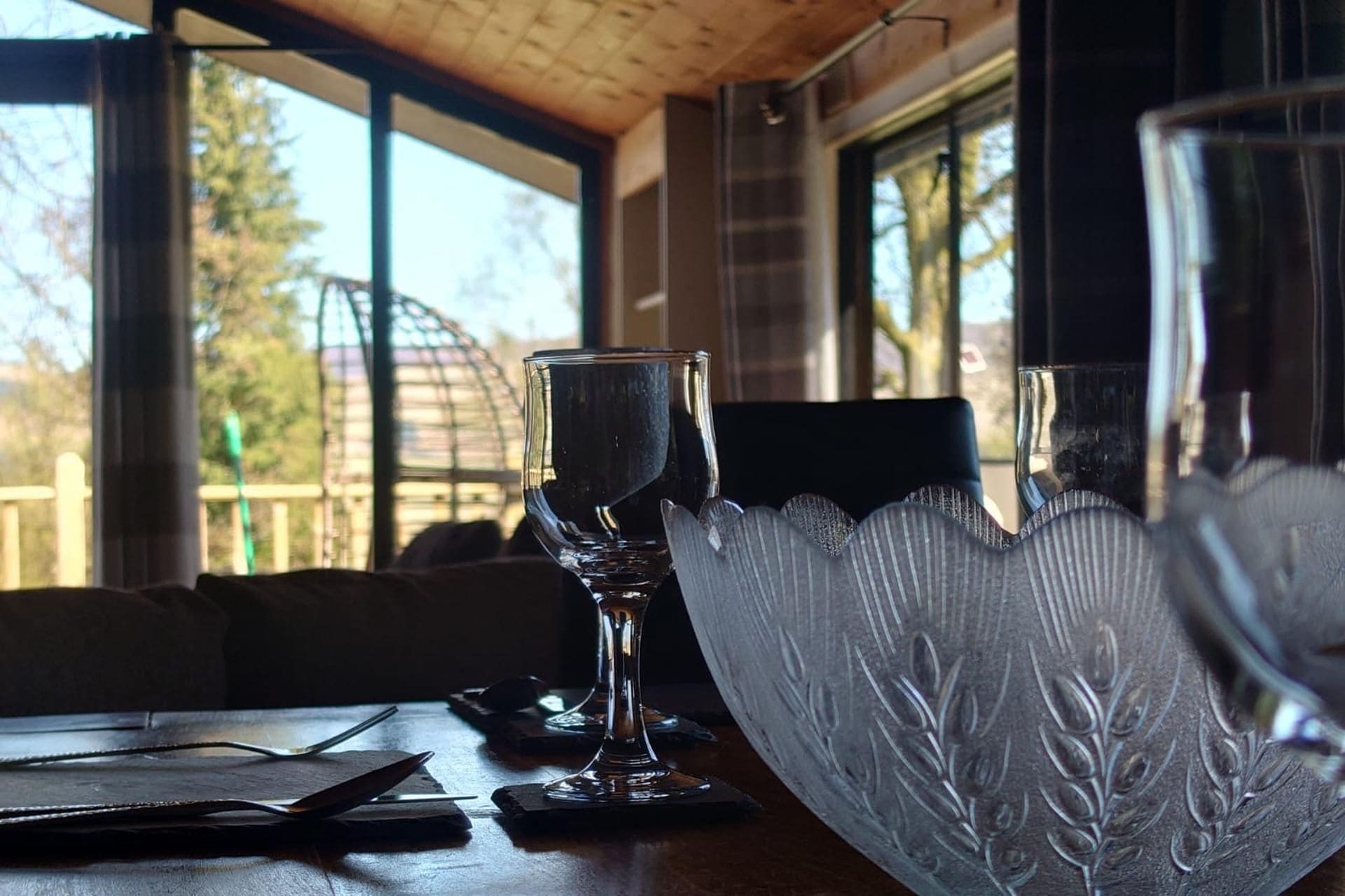 Une table avec deux verres transparents et un saladier décoratif, le tout placé devant une fenêtre donnant sur des arbres.