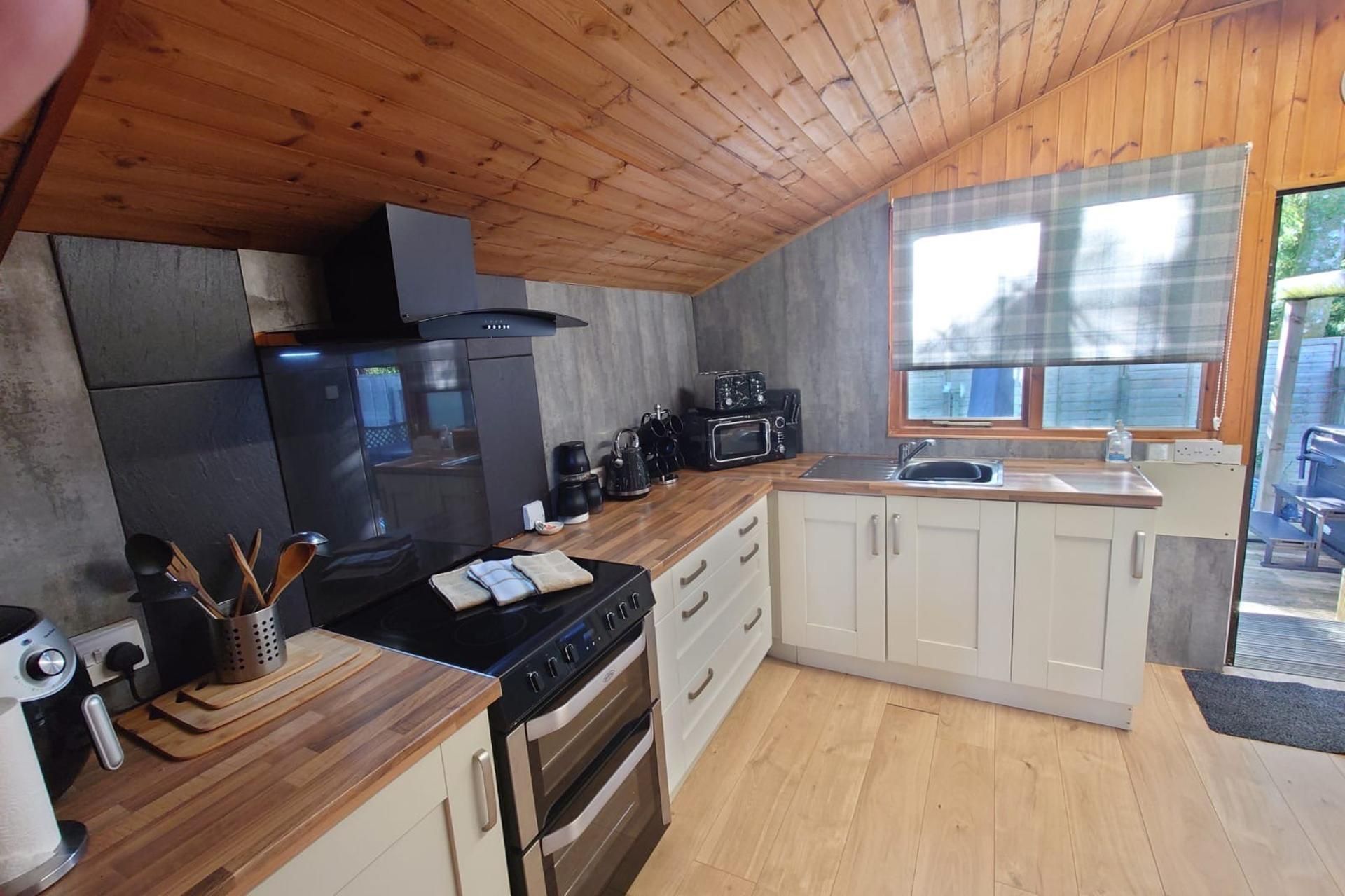 A compact kitchen with a wood ceiling, a black stove, a microwave, and a sink.