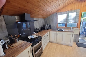 Cocina compacta con techo de madera, estufa negra, microondas y pileta.