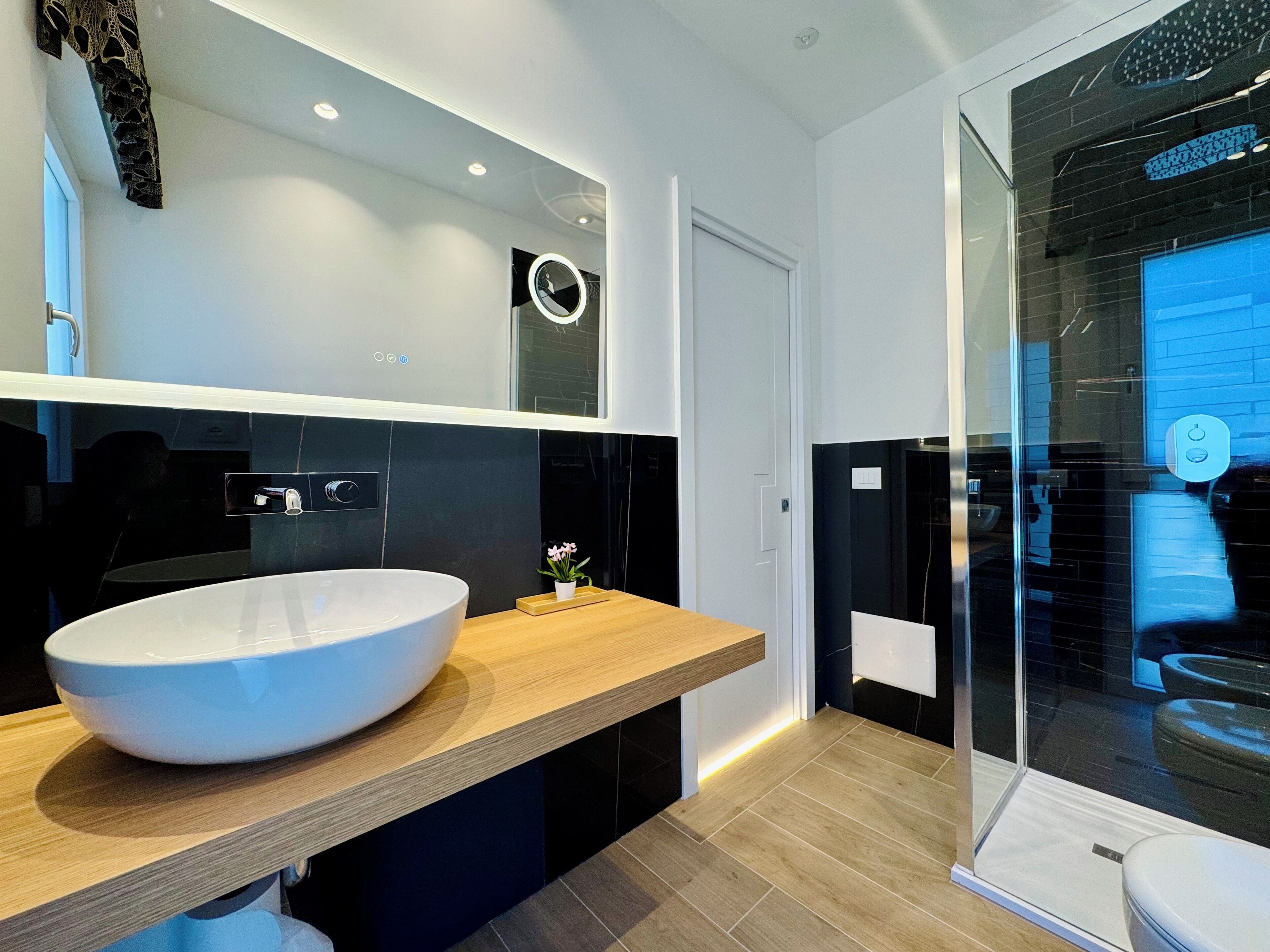 Un baño moderno con un lavamanos grande de color blanco, una encimera de madera, un espejo y un box de ducha de vidrio.