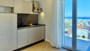 Une cuisine moderne dotée d’une cuisinière, d’un évier et de placards intégrés. Une grande fenêtre offre une vue sur le paysage urbain et la mer.