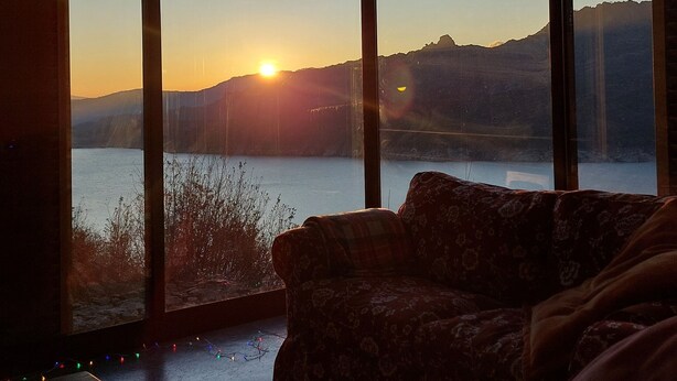 A room with a large window overlooking a body of water and distant mountains during sunset. - Brioso Cutlery House (Outeiro)