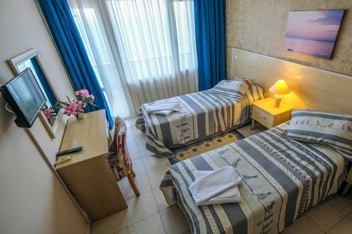 Ein Hotelzimmer mit zwei Betten, einem Schreibtisch, einem Sessel, einem Fernseher und einem Bild an der Wand.