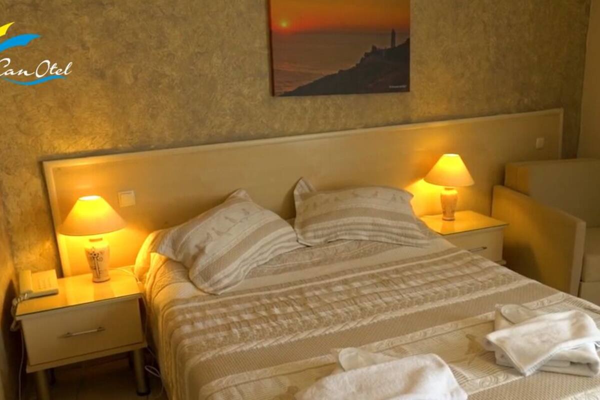 Ein Hotelzimmer mit einem Bett, zwei Nachttischlampen, einem Sessel und einem Sonnenuntergangsbild an der Wand.