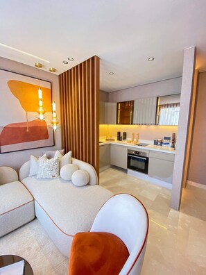 A modern living room with a sofa, a coffee table, and a red chair. There is a kitchen area with a sink and stove in the background.