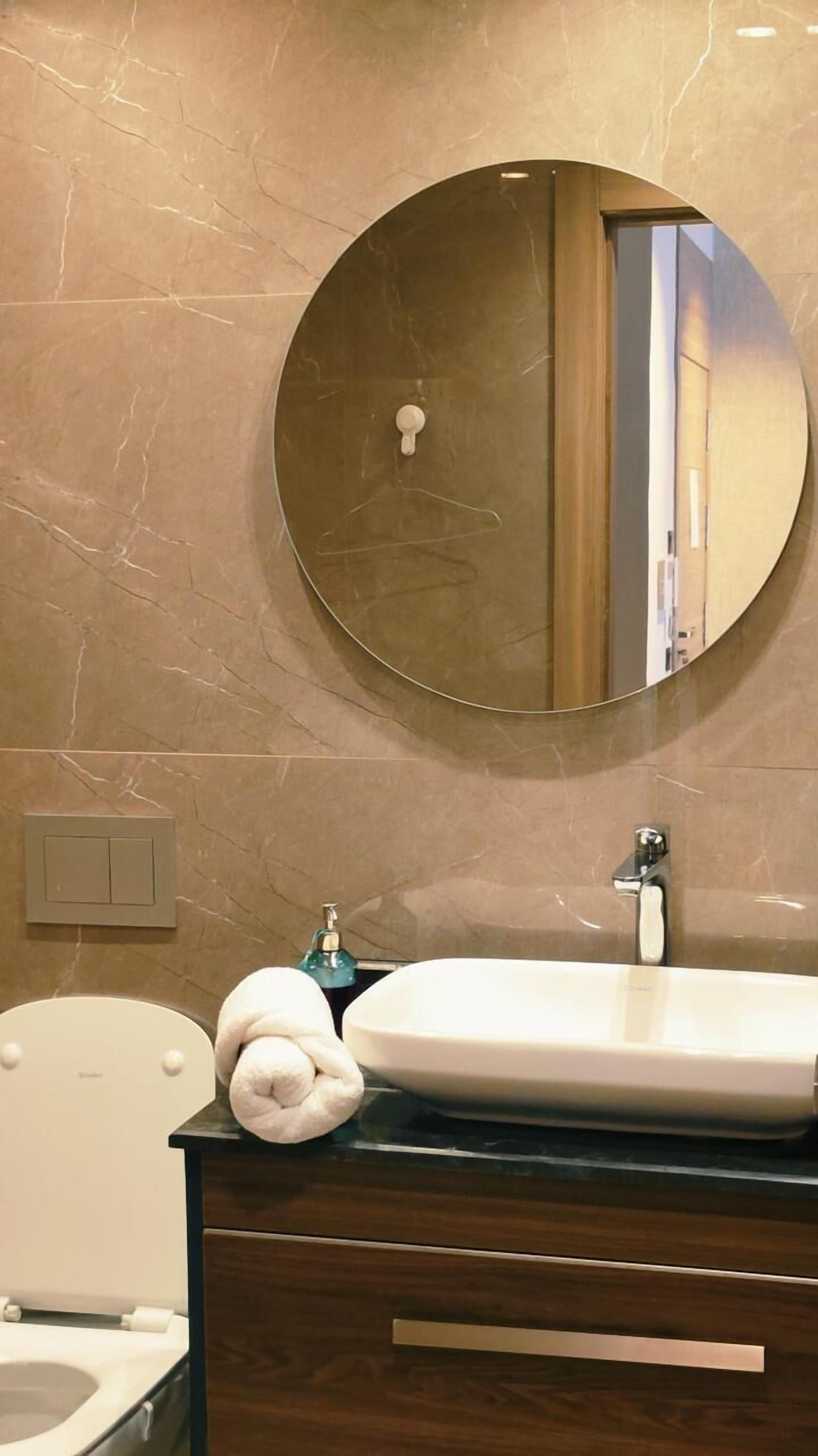 A bathroom with a round mirror, a sink, a toilet, and a towel.