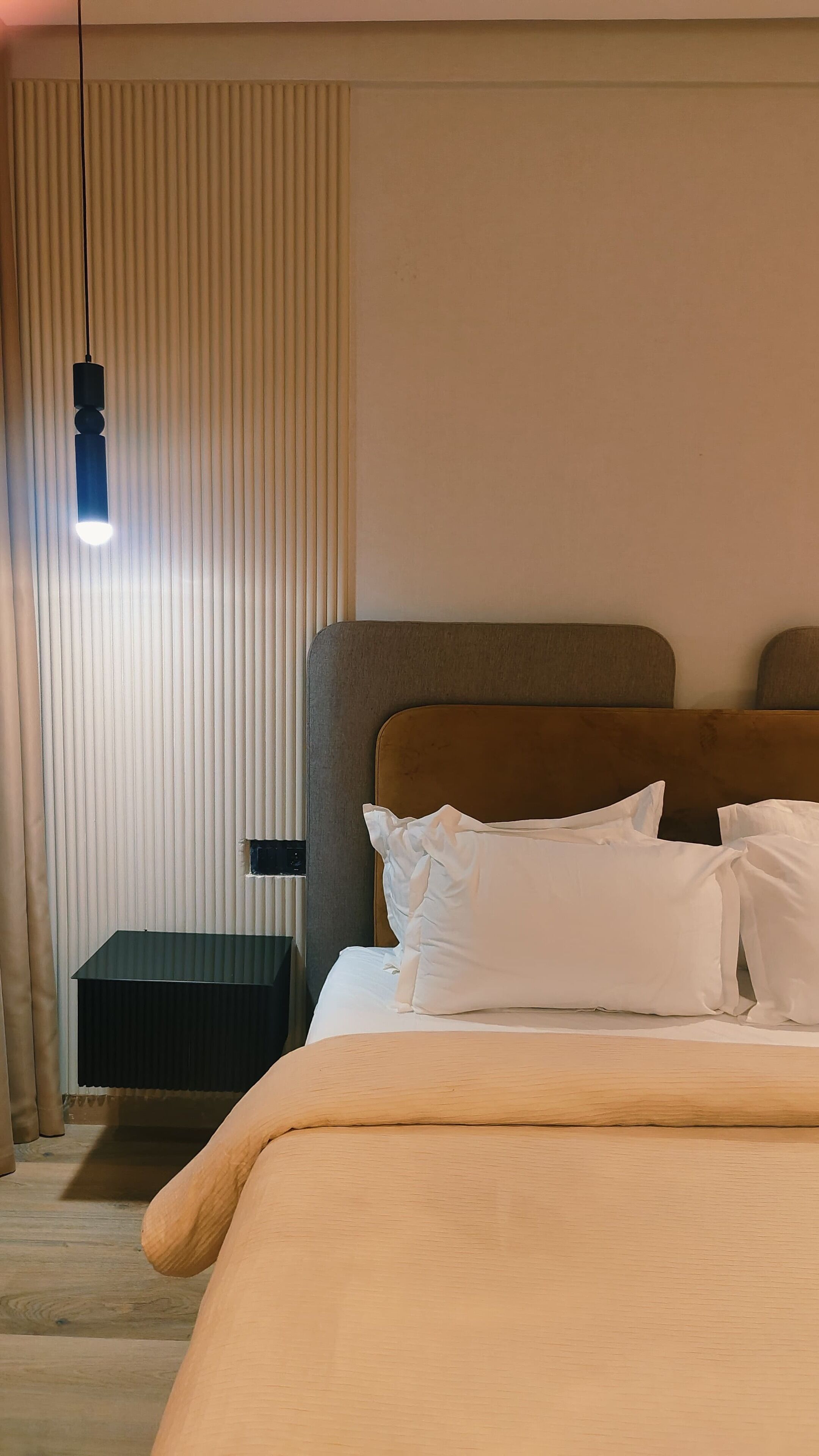 Una cama bien hecha con sábanas blancas, una mesita de noche oscura y una lámpara colgante.