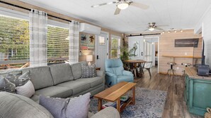 A spacious living area with a grey sofa, a blue armchair, a wooden coffee table, and a dining area with a wooden table and metal chairs. - 2BR Home, Private Heated Pool, 4 Bikes, Beach Access (Santa Rosa Beach)