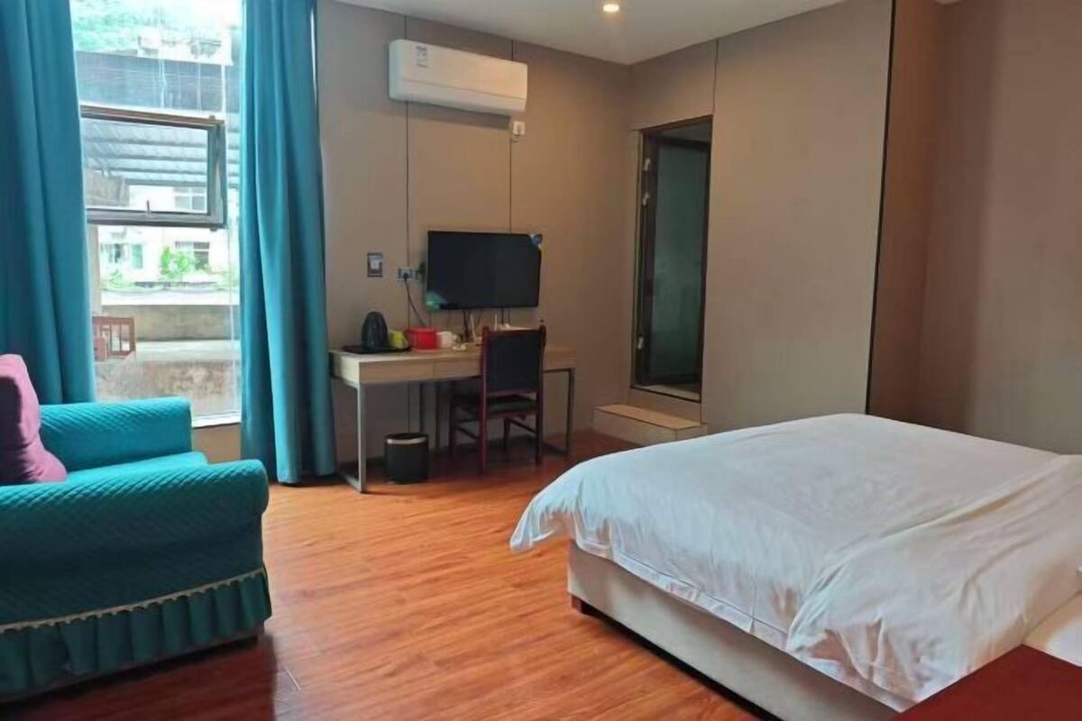 Een hotelkamer met een bed, een bureau met stoel, een televisie en een raam met gordijnen.
