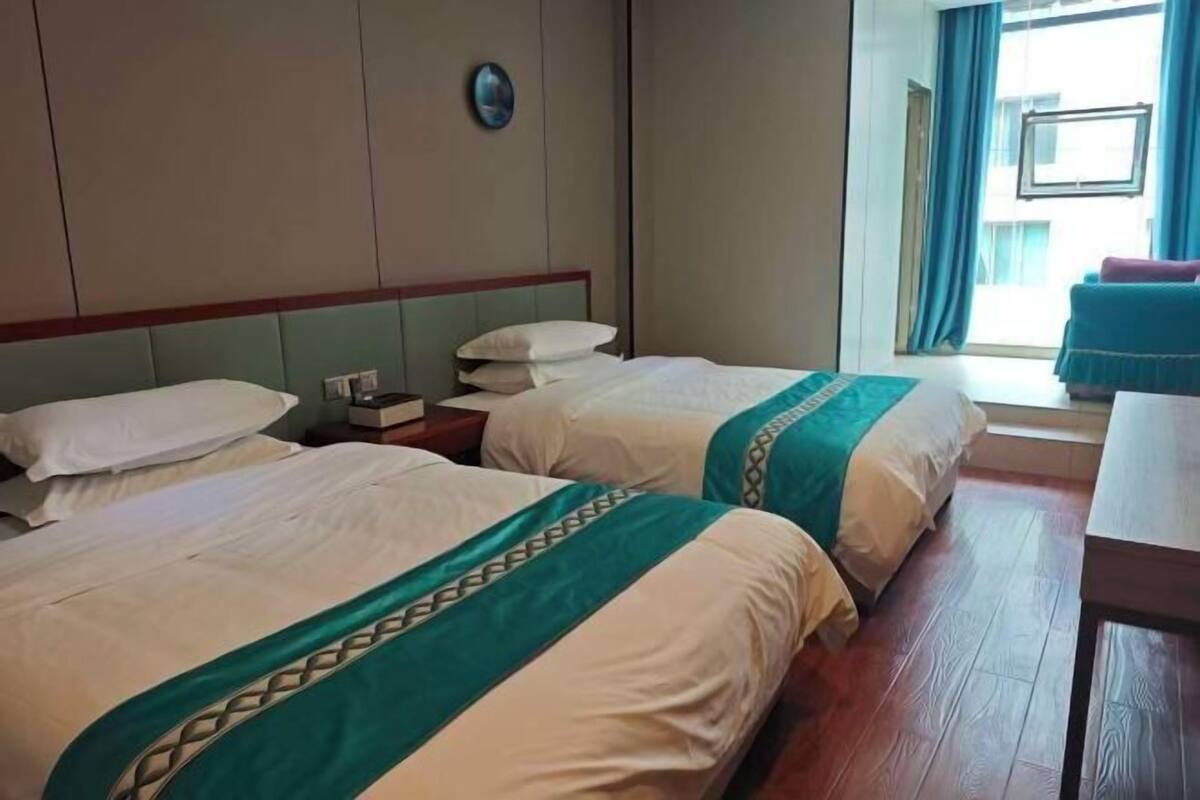 Een hotelkamer met twee bedden, een houten vloer, een raam met gordijnen en een klein tafeltje.