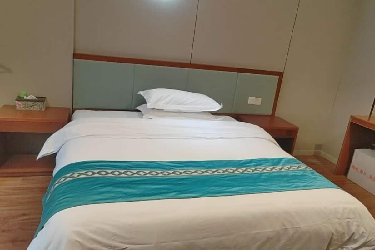 Una habitación de hotel con cama, mesita de noche, cabecero de madera y otra mesita auxiliar.