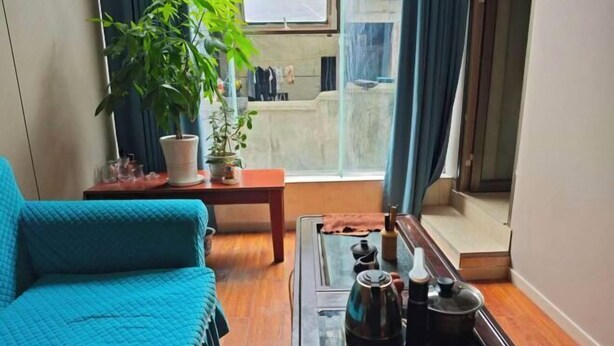 A room with a sofa, a small table with a kettle, a potted plant, and a view through a glass door. - Asbestos Jiayi Hotel (Shimian)