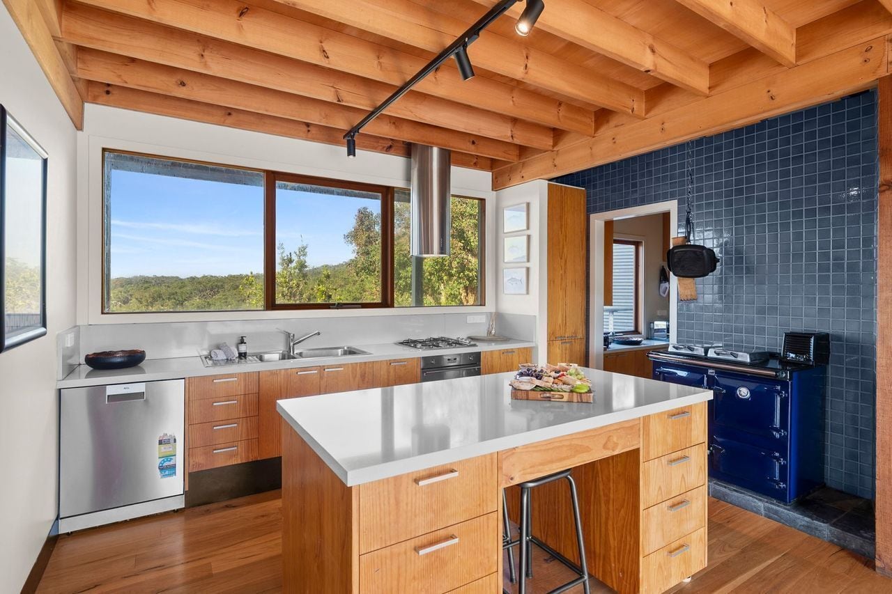 A modern kitchen with wooden cabinets, a stainless steel refrigerator, a large island, and a view of the outdoors.
