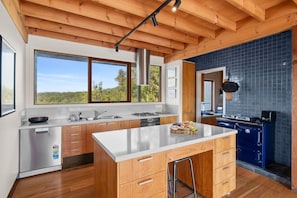 A modern kitchen with wooden cabinets, a stainless steel refrigerator, a large island, and a view of the outdoors. - Janacwal - Where Escape Meets Adventure (Bells Beach)