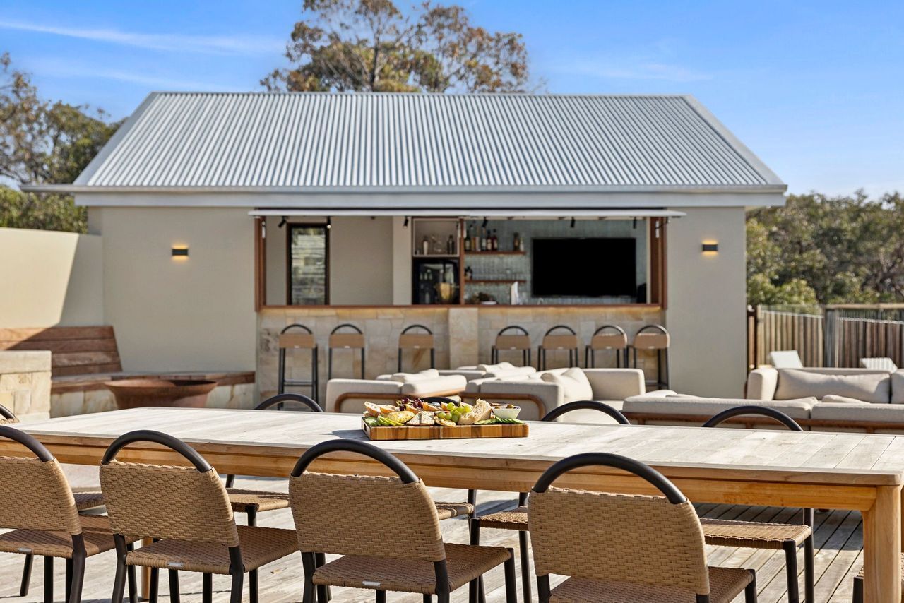 An outdoor dining area with a bar, wicker chairs, and a wooden table.
