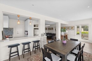 A modern kitchen with a bar area, a dining table with chairs, and a living area with a sofa and coffee table.