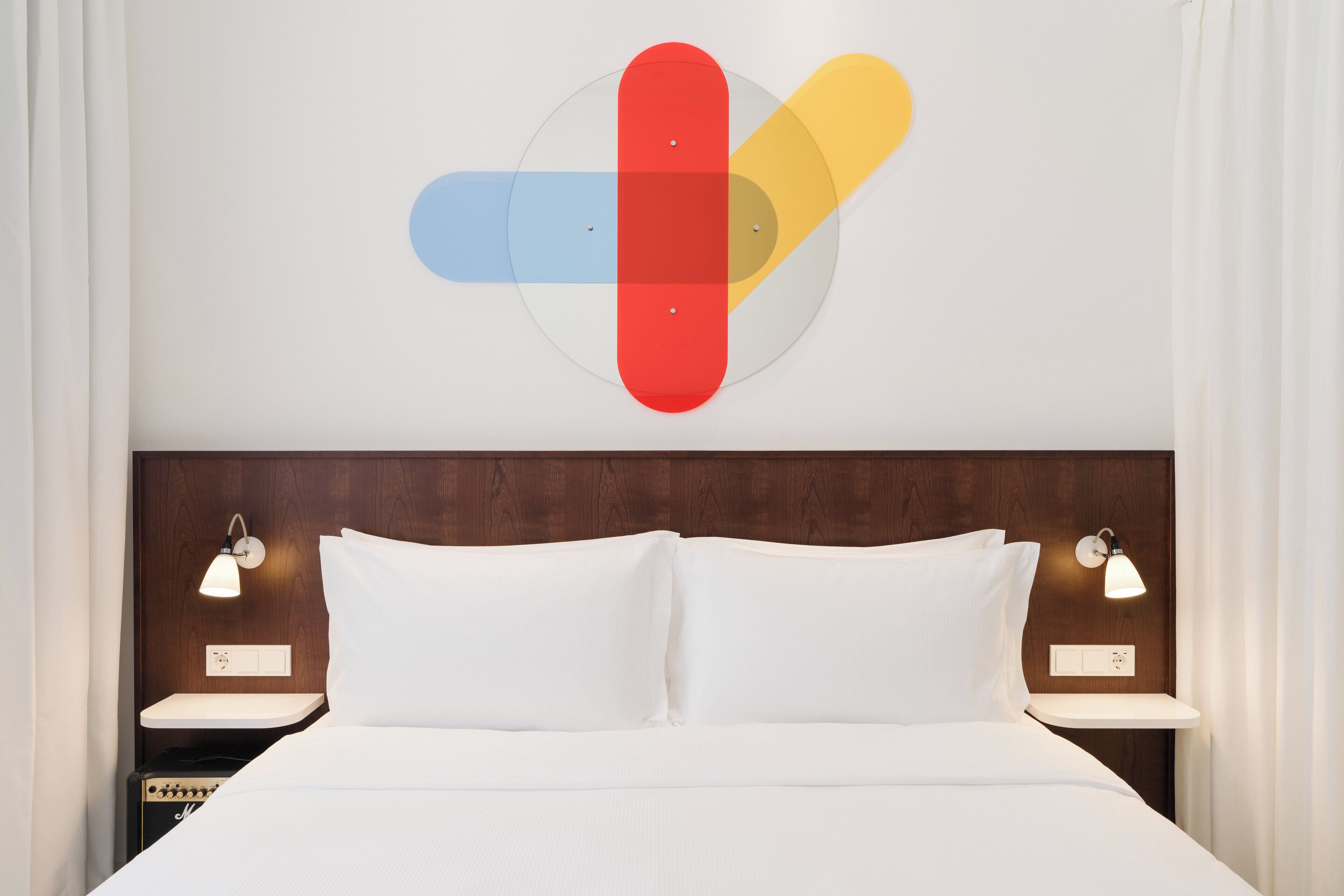 Ein modernes Hotelzimmer mit einem großen Bett, weißer Bettwäsche, zwei Nachttischen mit Lampen und einem hölzernen Kopfteil.