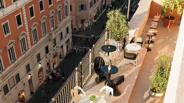 A rooftop terrace with outdoor seating and a view of a busy street below.