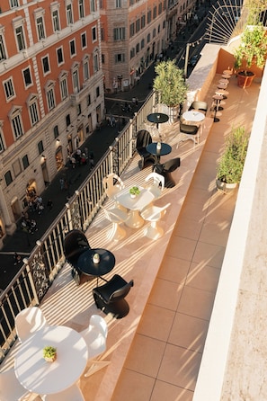 A rooftop terrace with outdoor seating and a view of a busy street below.