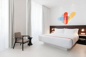 Una camera d'albergo moderna con un grande letto, una sedia, un tavolino e un comodino con una lampada.
