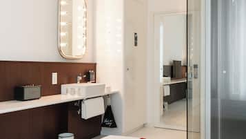 A modern bathroom with a vanity, a large mirror with lights, a radio, and a glass shower enclosure.