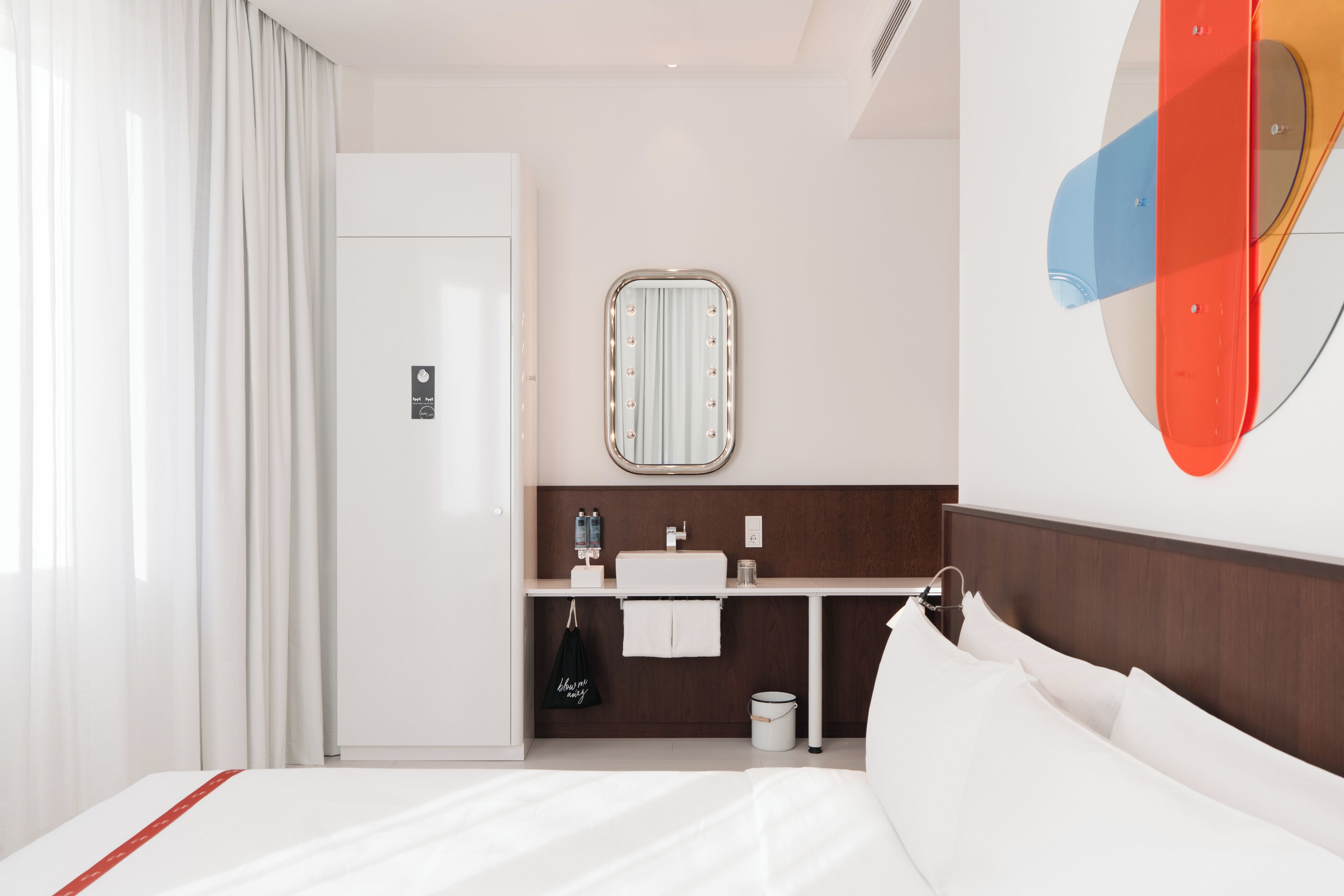 A hotel room with a bed, a vanity with a mirror, a small table, and a door.