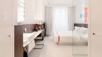 Une chambre d’hôtel moderne équipée d’un lit, d’un bureau, d’un miroir et d’une salle de bain.