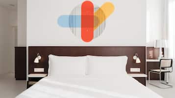 Een hotelkamer met een bed, een nachtkastje met een lamp, een kunstwerk aan de muur en een raam met gordijnen.