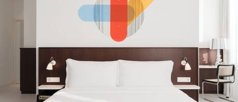 A hotel room with a bed, a nightstand with a lamp, a wall art piece, and a window with curtains.