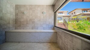 A bathroom with beige tiles, a window with a view of a residential area, and a metal railing. - Bz95 Cond. Viva Búzios Casa 4 quartos (Búzios)