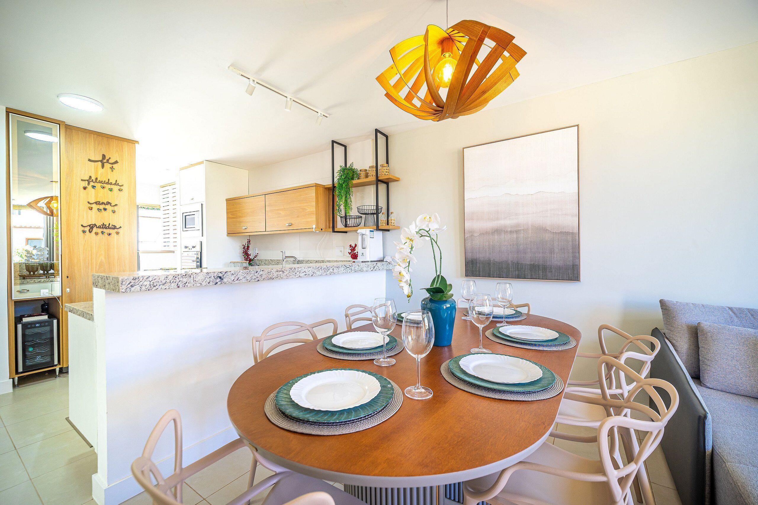 A dining area with a round table set for four, surrounded by chairs. There is a kitchen area with wooden cabinets and a countertop visible in the background.