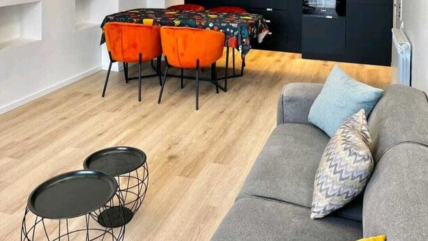 En moderne stue med en grå sofa, et sofabord og et spiseområde med orange stole.