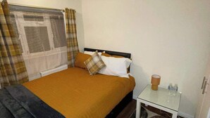 Ein Schlafzimmer mit Bett, Nachttisch, Lampe und einem Fenster mit Vorhängen.