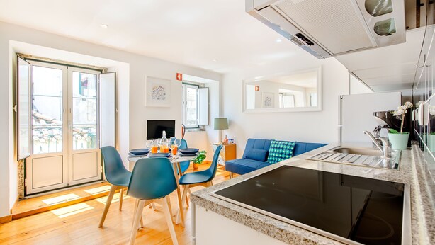 A modern kitchen with a built-in stove, dining area with chairs and a table, and a blue sofa. - Charming Flat in Alfama (Lisbon)
