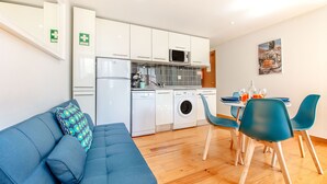 A compact living space with a kitchenette, a dining area with a table and chairs, and a sofa with a patterned pillow. - Charming Flat in Alfama (Lisbon)
