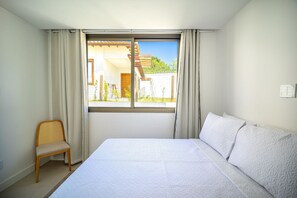 A bedroom with a large bed, a chair, and a window with curtains. - Bz96 Linda casa 4 quartos (Búzios)