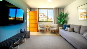 A modern living room with a sofa, two armchairs, a TV, and a large window.