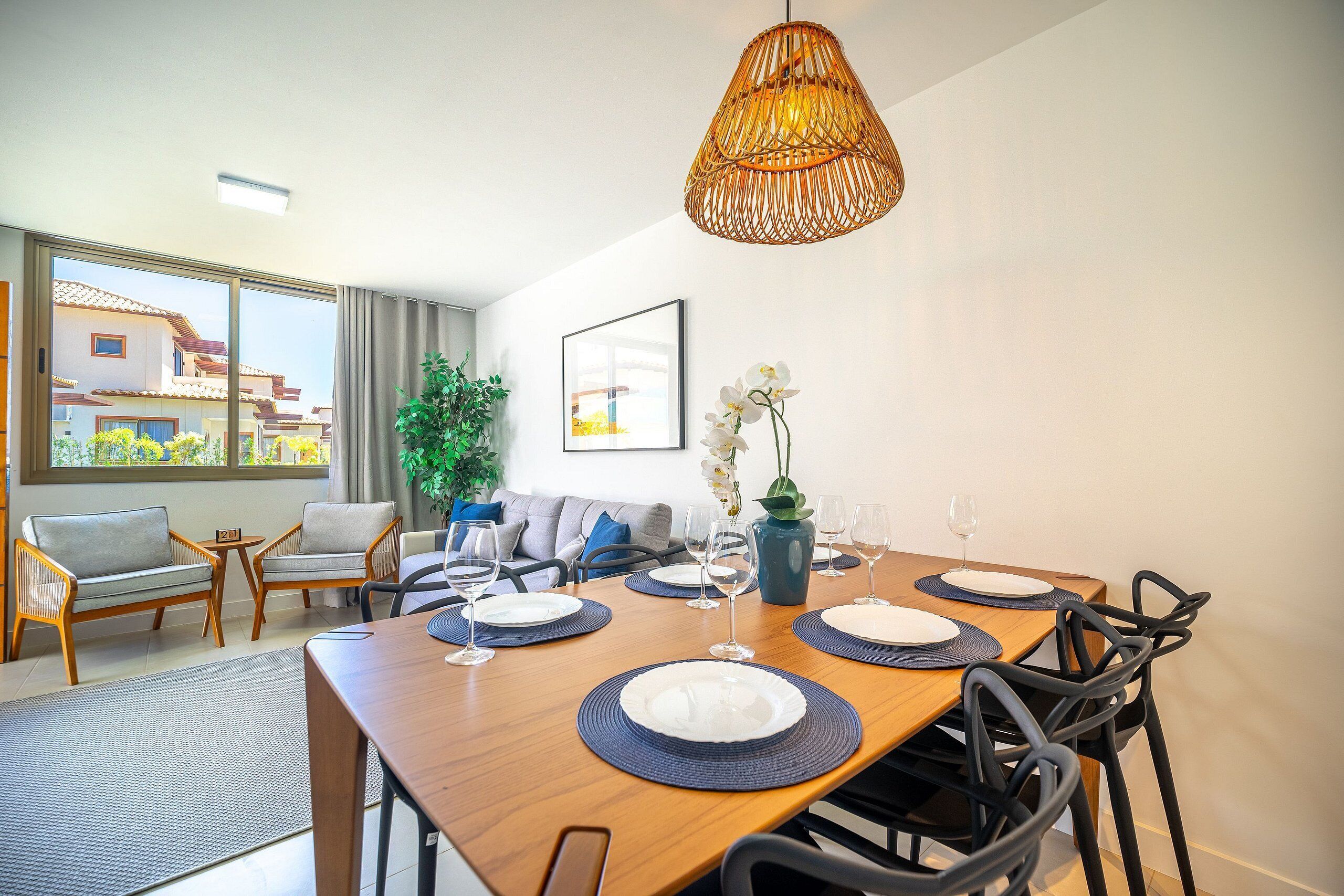 A dining area with a wooden table set for six, surrounded by black chairs. There is a large window with a view of buildings outside.