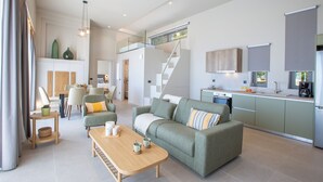 Una sala de estar moderna con sofá, una mesita de centro y un comedor. Se ve una escalera que sube a un nivel superior.