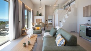 Una sala de estar moderna con sofá, mesa de centro y sillones. Se ve una escalera que sube a un nivel superior.