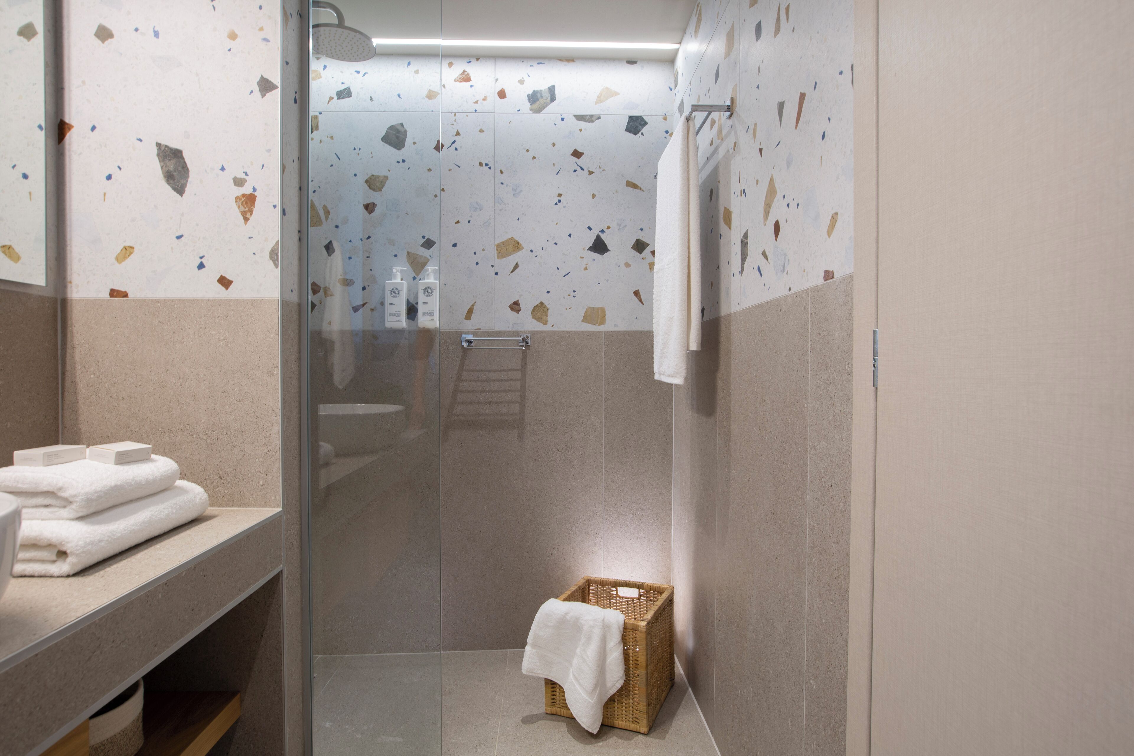 Un baño moderno con cabina de ducha de vidrio, una cesta de madera con una toalla y una pila de toallas en un estante.