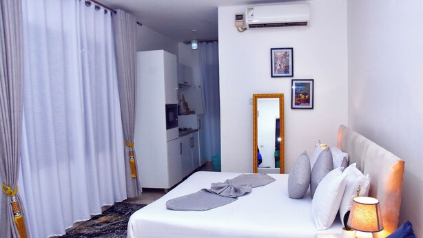 A hotel room with a bed, a bedside lamp, a mirror, and a small table. - Good deeds Stay (Entebbe)