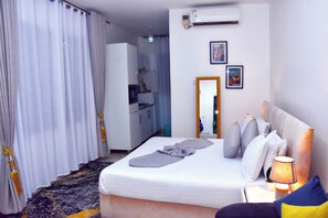 A hotel room with a bed, a bedside lamp, a mirror, and a small table. - Good deeds Stay (Entebbe)