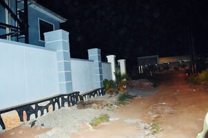 A nighttime view of a building with a blue exterior and a dirt path leading to a gated entrance.