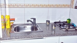 A kitchen with a stainless steel sink, a gas stove, and various kitchen items like bottles and a cup. - Good deeds Stay (Entebbe)