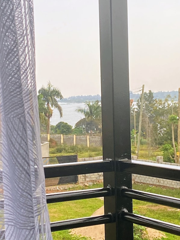 Vista desde una ventana con barandilla de metal, que da a una masa de agua, palmeras y una costa distante.