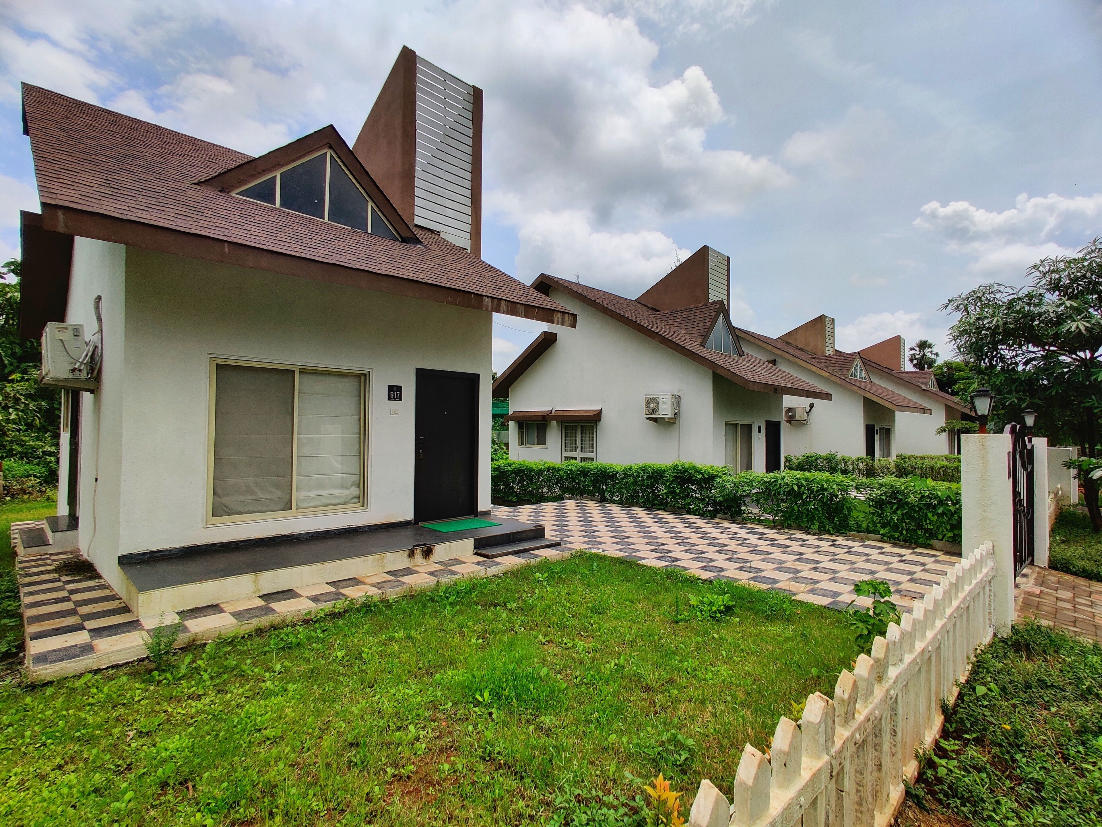 A row of modern houses with a checkered driveway, a green lawn, and a white picket fence.