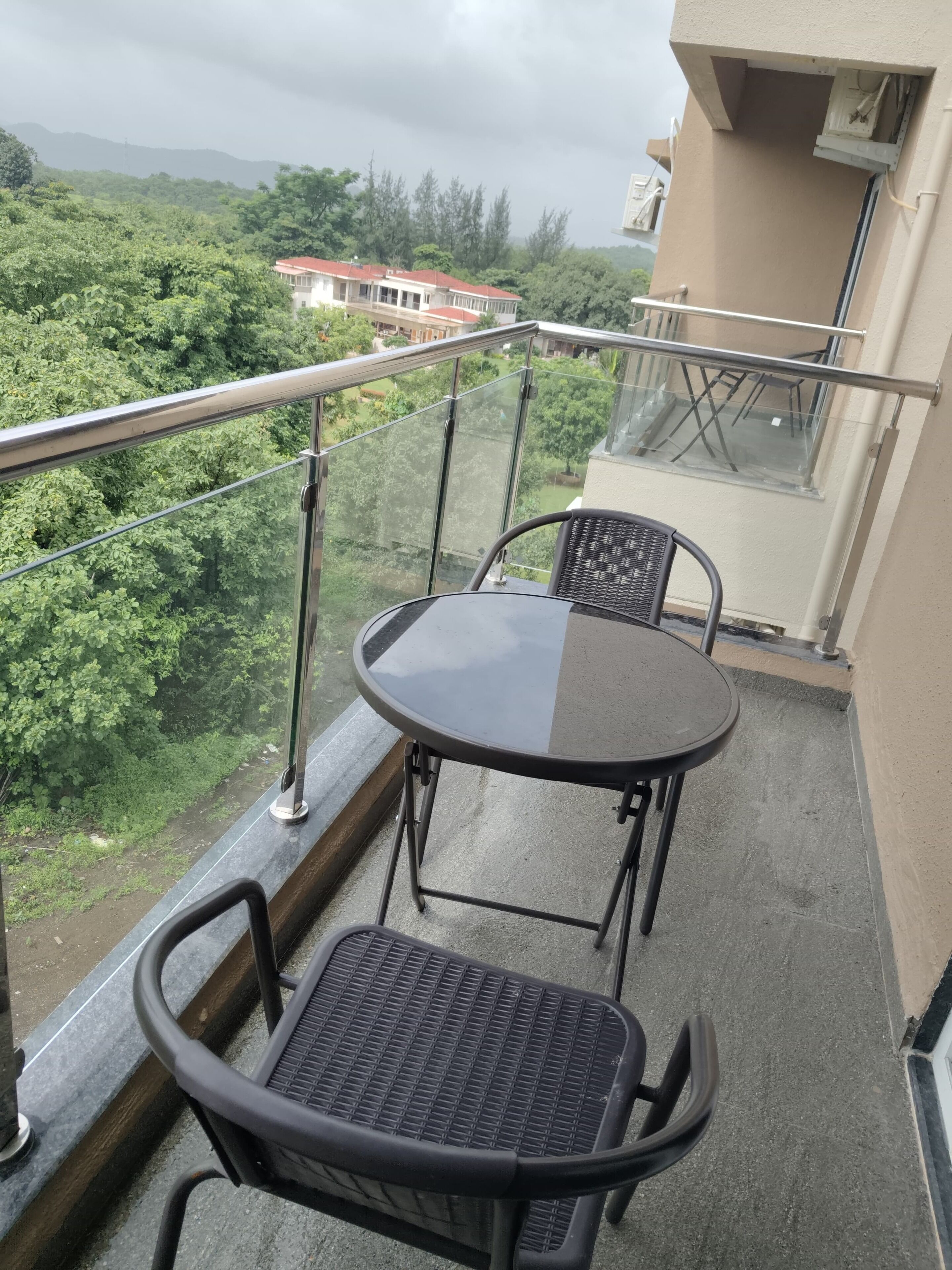 Un balcón con una mesa y dos sillas, con vistas a un paisaje verde exuberante y edificios a lo lejos.