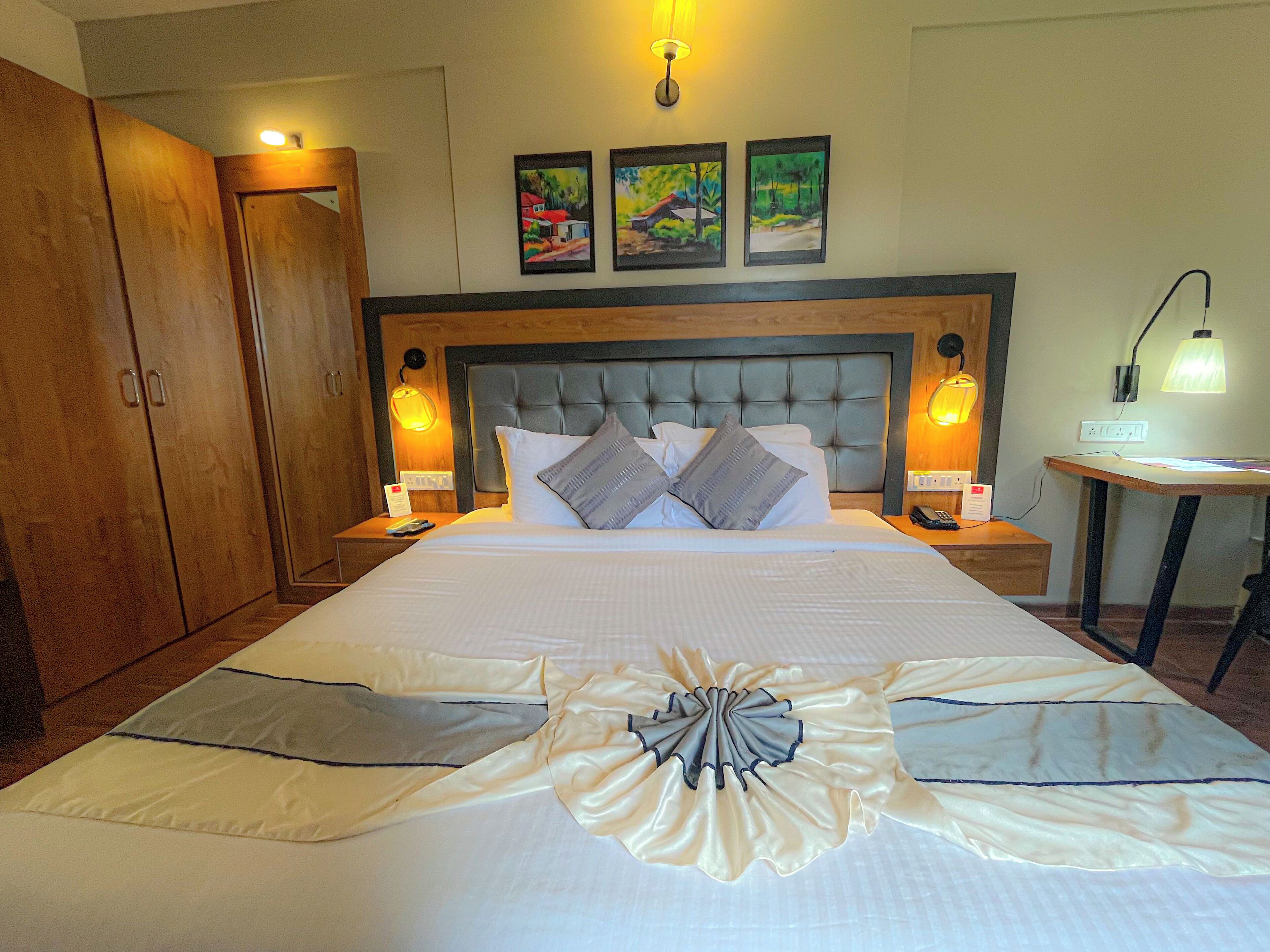 A hotel room with a large bed, wooden wardrobe, bedside lamps, and framed artwork on the wall.