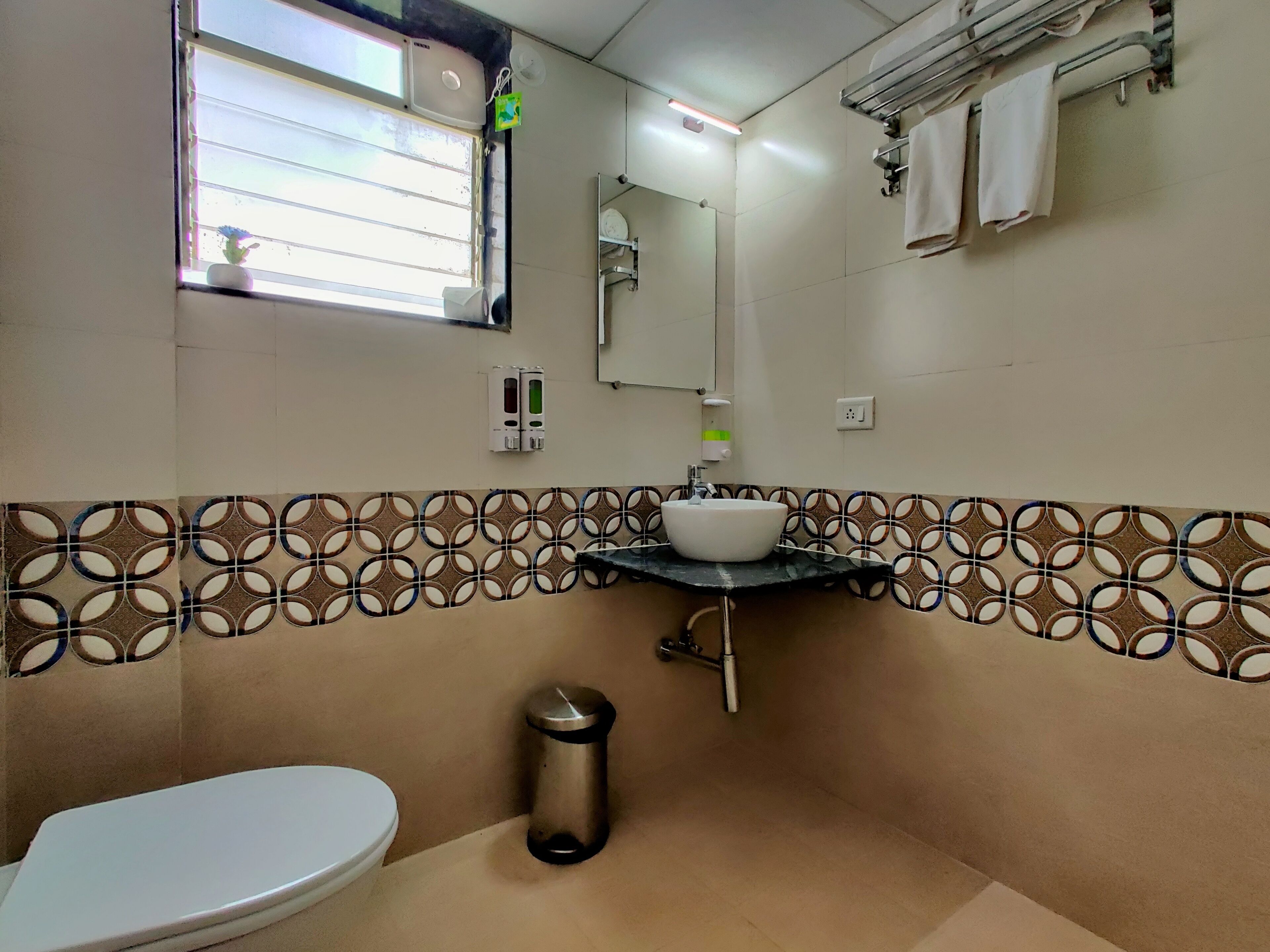 Un baño con inodoro, lavamanos, espejo, toallero y un cesto de basura.